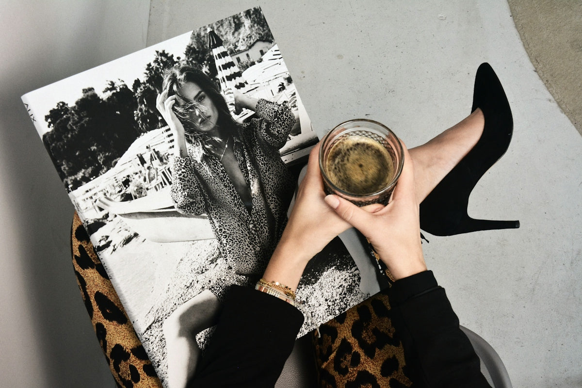 A person holding a glass of coffee over a black and white fashion magazine